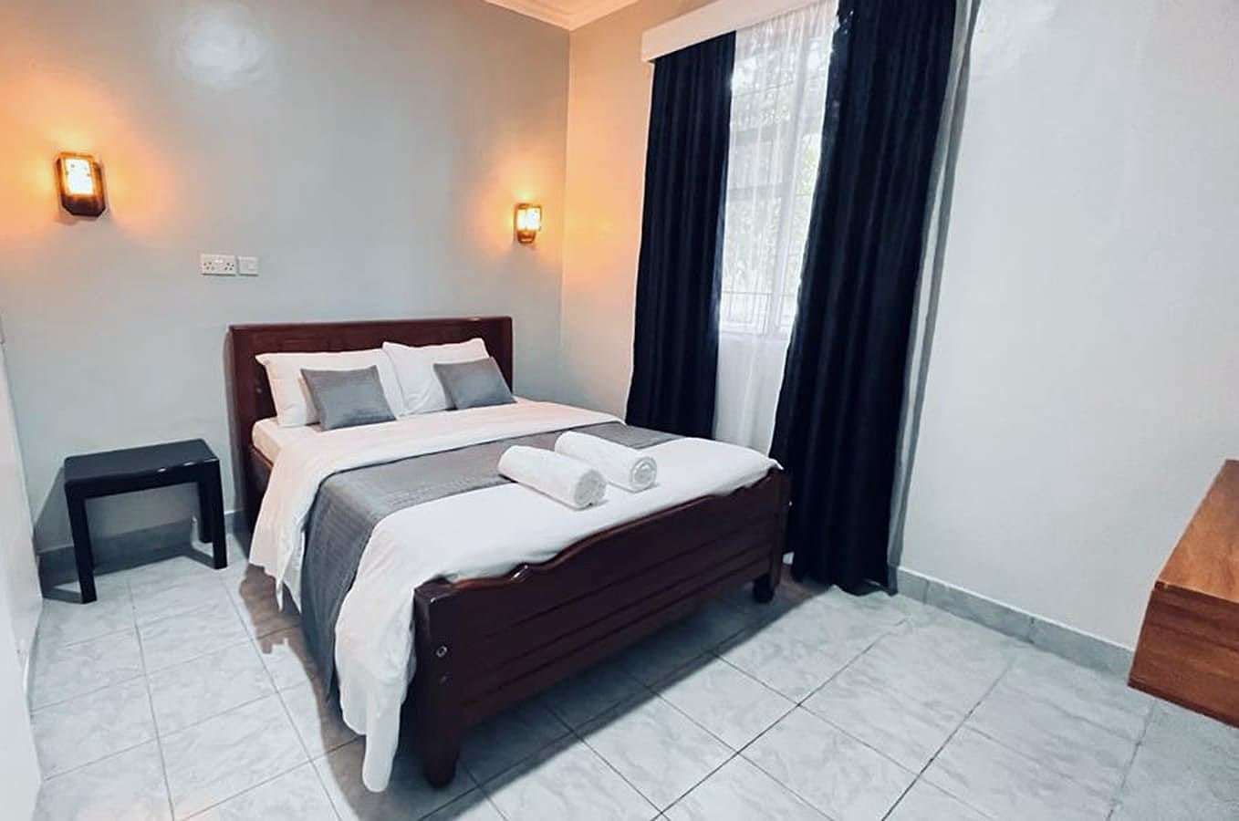 Standard room with a wooden double bed, white linen and dark curtains