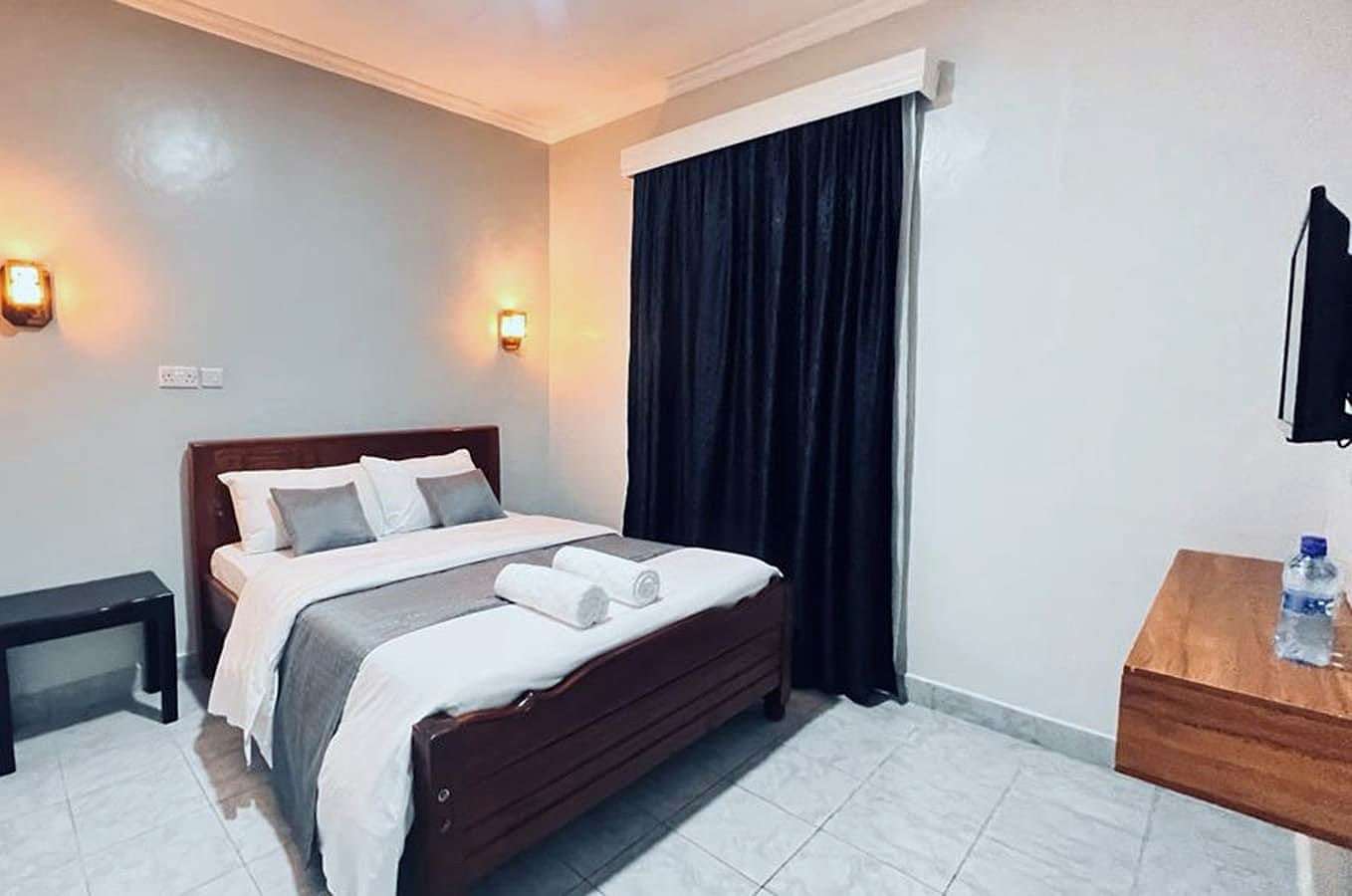 Standard room bed with rolled white towels and bedside lights