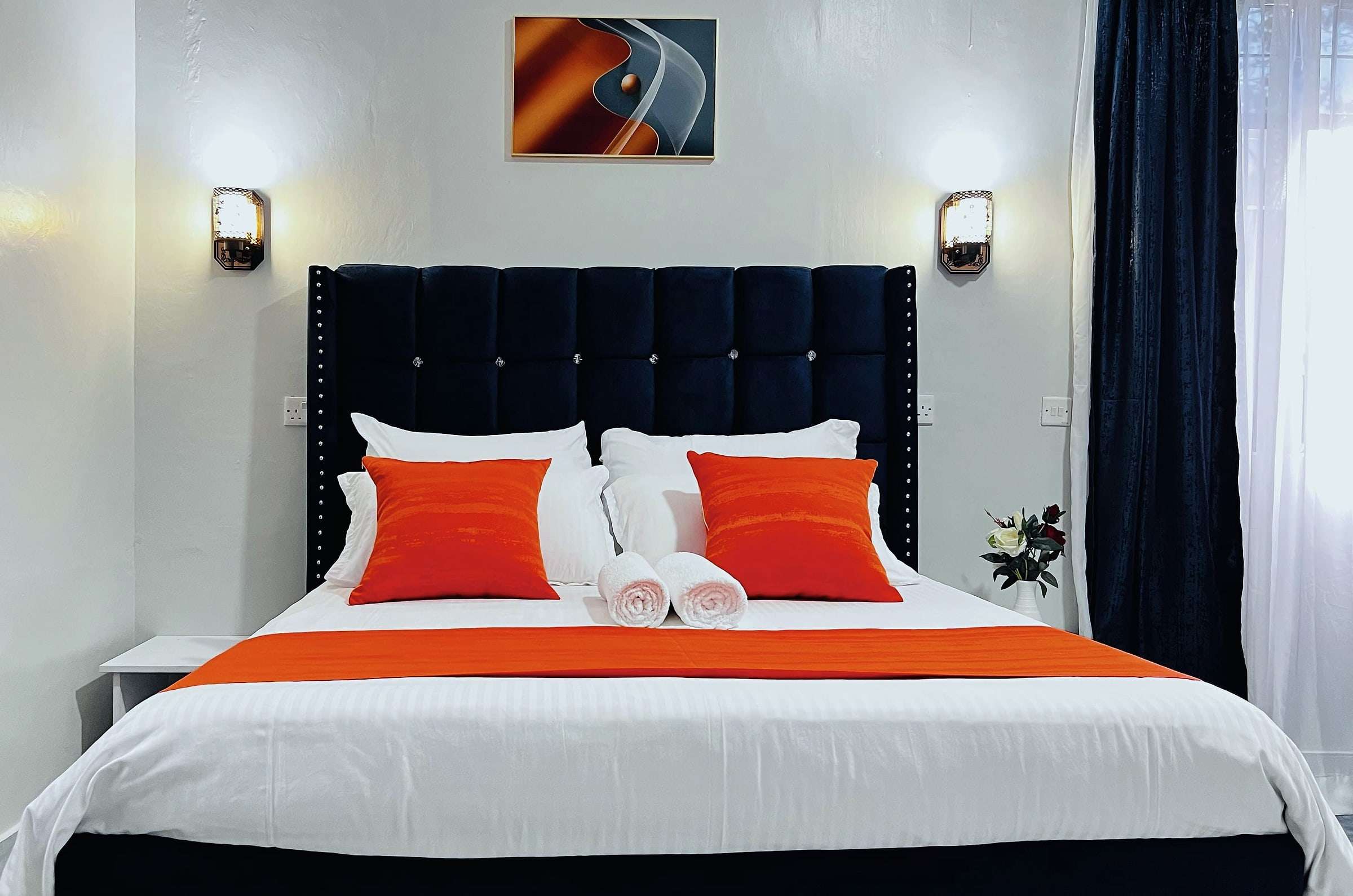 VIP room bed with crisp white linen, rolled towels and orange cushions